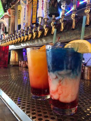 Two drinks are sitting on a bar next to the taps.