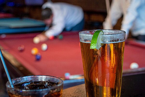 A glass of beer on the table near some pool balls